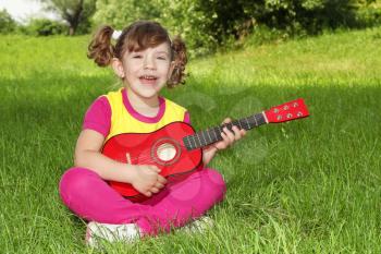 little girl sitting on grass play guitar and sing