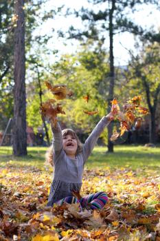 happy little girl throws leaves in autumn park