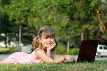 happy little girl with laptop lying on grass
