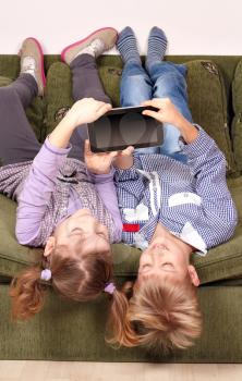 little girl and boy lying upside down on bed and play with tablet