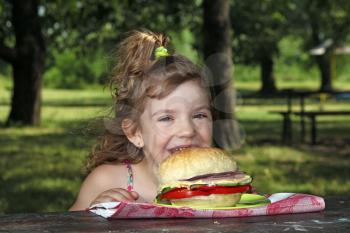 hungry little girl eat big sandwich in park
