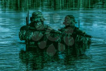 Pair of soldiers in action during river raid in the jungle in the night waist deep in the water and mud and covering each other