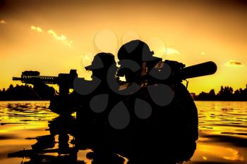 Silhouette of special forces with rifle in action during river raid in the jungle waist deep in the water. Proflie side view, half length