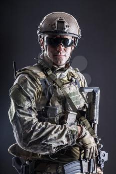 Half length studio shot of special forces soldier in field uniforms with weapons, portrait on black background. Protective goggles glasses are on