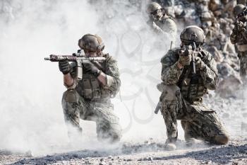Team squad of special forces in action in the desert among the rocks covered by smoke screen