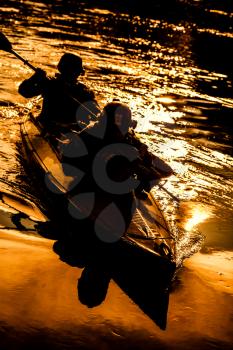 Silhouette of special forces men paddling army kayak. Boat moving calmly across the river, diversionary mission, sunset dusk