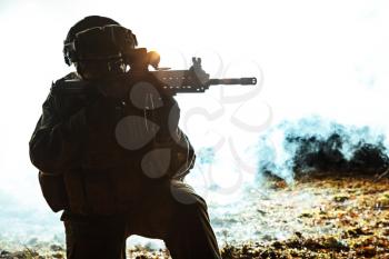 Black silhouette of soldier in the smoke moving in battle operation. Back light, cropped, toned and colorized