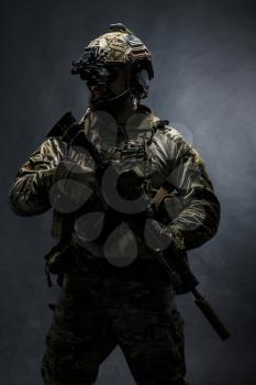 Bearded soldier in Combat Uniforms with weapon, plate carrier and combat helmet are on. Studio shot, dark background