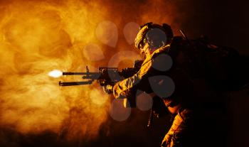 Security forces operator in Combat Uniforms with machine gun, shooting in the face of danger. Facing enemy, he is ready to protect the nation. Gun blazing. Studio contour silhouette shot, backlight, profile side view