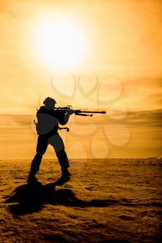 Silhouette of soldier with sniper rifle standing under scorching sun in the mountains
