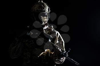 Army soldier in Protective Combat Uniform holding Special Operations Forces Combat Assault Rifle. Studio shot, dark contrast, cropped, black dark background, contour shot