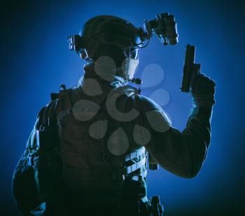 Army elite forces soldier, police special operation, counter terrorist team member in tactical ammunition with hidden behind mask identity, standing backwards with pistol in hand, low key studio shoot