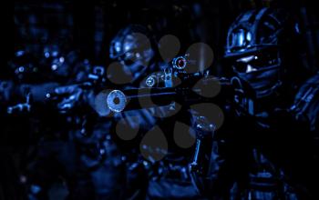 Police special operations, quick reaction tactical group members in black uniforms, helmet and hidden behind masks faces standing in line, aiming with assault rifles on terrorism response operation