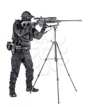 Studio shoot of police special forces sniper in black blank uniform and hidden behind mask identity aiming with telescopic optical sight on sniper rifle mounted on tripod, isolated on white background