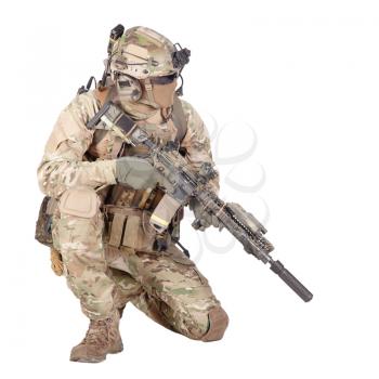 Army special forces infantry in battle uniform, radio headset on helmet, armed service rifle, standing on knee, waiting in ambush, patrolling area, observing territory studio shoot isolated on white