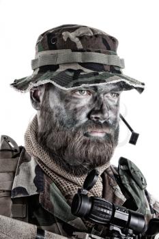 Shoulder studio portrait of commando soldier, modern mercenary, professional soldier with black camouflage paint on bearded face, tactical radio headset with microphone, isolated on white background