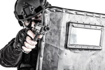 Police quick reaction team, special operations tactical group member in mask, helmet and goggles, hiding behind ballistic shield, aiming with pistol in firefight with dangerous criminals or terrorists