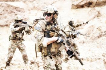Group of well equipped US army commandos armed with assault rifles, moving through sandy terrain or desert. Military reconnaissance team secret operation, special forces mission on enemy territory