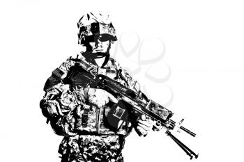 Black and white studio portrait of US Armed Forces soldier in protective camouflage, helmet and tactical sunglasses holding light machine gun and looking in camera desaturated, isolated on white background