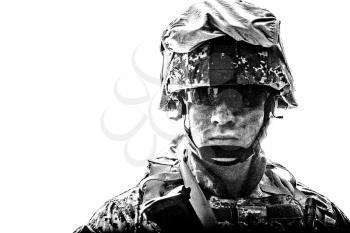 Shoulder black and white portrait of modern army infantry soldier with dirty face in digital camouflage battle uniform, combat helmet, tactical sunglasses looking at camera desaturated, isolated on white background