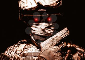 Special operations forces soldier in combat helmet with terrible burning red eyes posing with sidearm service pistol in hand. Brown tone, high contrast, cropped on black background