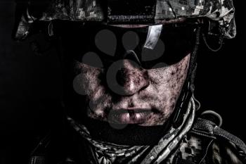Cropped close up portrait of US special operations forces soldier, marine raider, modern combatant in helmet and glasses with dirty face after difficult military mission or battle looking at camera