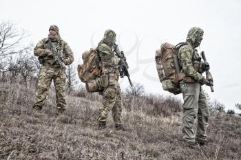 Army team members, military mercenary group in various types camouflage uniform, armed service rifles, observing territory from hill, patrolling area during mission
