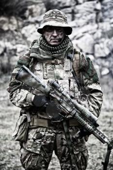 Portrait or commando veteran, experienced and skilled mercenary, army special forces sniper, counter-terrorism squad marksman in camouflage combat uniform, standing with sniper rifle in rocky area