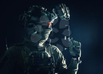 Side view portrait of army soldier, modern combatant, special forces fighter in helmet, night-vision device, radio headset, hiding identity behind mask, armed service pistol, low key studio shoot