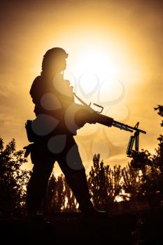 Silhouette of young soldier in military helmet against the sun