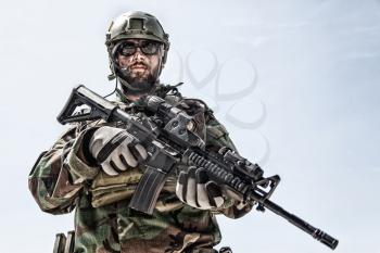 Private military company mercenary, brutal looking special forces fighter in battle uniform and plate carrier, wearing radio headset and sunglasses, holding service rifle in hands, ready to fight