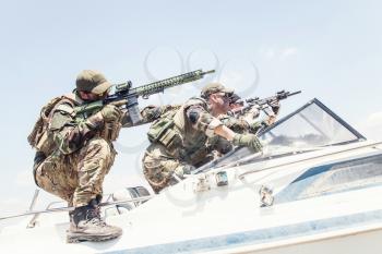 Anti terrorist squad fighters, SEALs team soldiers armed service rifle with optical sigh and silencer, rushing on speed boat, screaming commands to comrades, chasing and attacking enemy on water