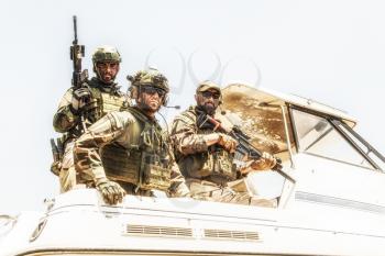 Army special operations soldiers, SEALs team, elite commando fighters group loaded with ammunition, wearing helmets and radio headset, armed assault rifles, standing together on speed boat stern