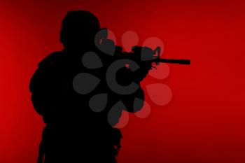 United states Marine Corps special operations command Marsoc raider with weapon aiming a gun. Silhouette of Marine Special Operator red background