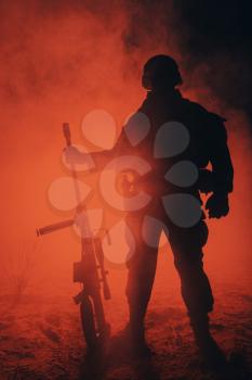 Army sniper with large caliber rifle standing in the fire and smoke. Backlit silhouette, toned image