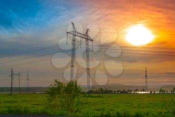 Electricity pylons and wires in a green field against evening sky