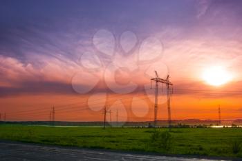 Electricity pylons and wires in a green field against evening sky