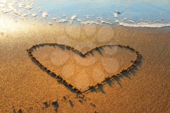 Heart drawn on the beach sand with sea foam and wave 