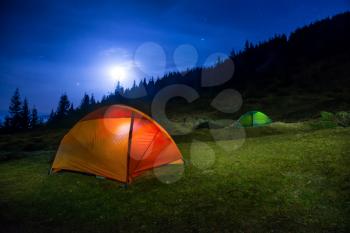 Two Illuminated orange and green camping tents under moon, stars at night 