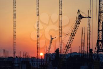Industrial landscape with silhouettes of cranes on the sunset background