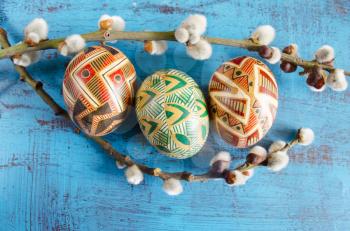 Easter colorful eggs and willow branches on blue wooden background. Springtime. Holiday card. Spring willow twigs with catkins and ornate eggs. Happy Easter. Still life with Pysanka. Easter background