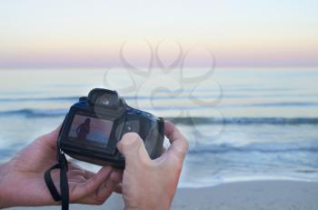 Hands of photographer holding a photo camera with a picture in the sea.