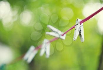 White plastic clothespins hanging on red rope with beautiful bokeh green background.