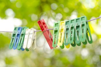 Plastic color clothespin hanging on rope, isolated on green bokeh background. Close-up, outdoor, depth of field. Colorful clothes pegs set.