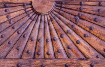 Ornate wooden pattern with metal rivets. Relief wooden part of old door with geometrical ornament in the form of the sun with rays.