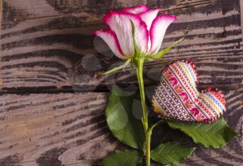 Beautiful rose on brown wooden background and fabric heart.