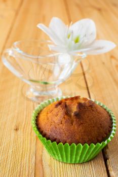 Muffin in the green paper cupcake holder and white flower in the glass on a wooden background, selective focus