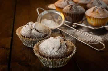 Vanilla and chocolate muffins, caster sugar, sieve for a baking on a dark background, selective focus, copyspace
