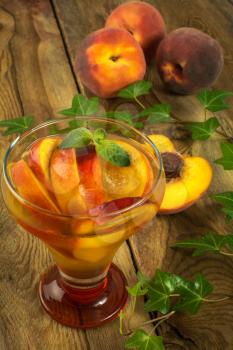 Peach drink in glass on a wooden background with peaches and ivy branch. Selective focus. The toning