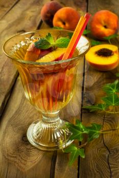 Refreshing drink, iced green tea with peaches and mint in a glass on a dark wooden background, close up, vertical, selective focus